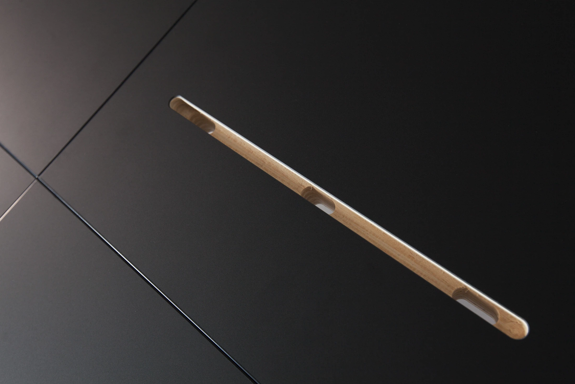 An angled tablet slot in a black surface, revealing the light wood core